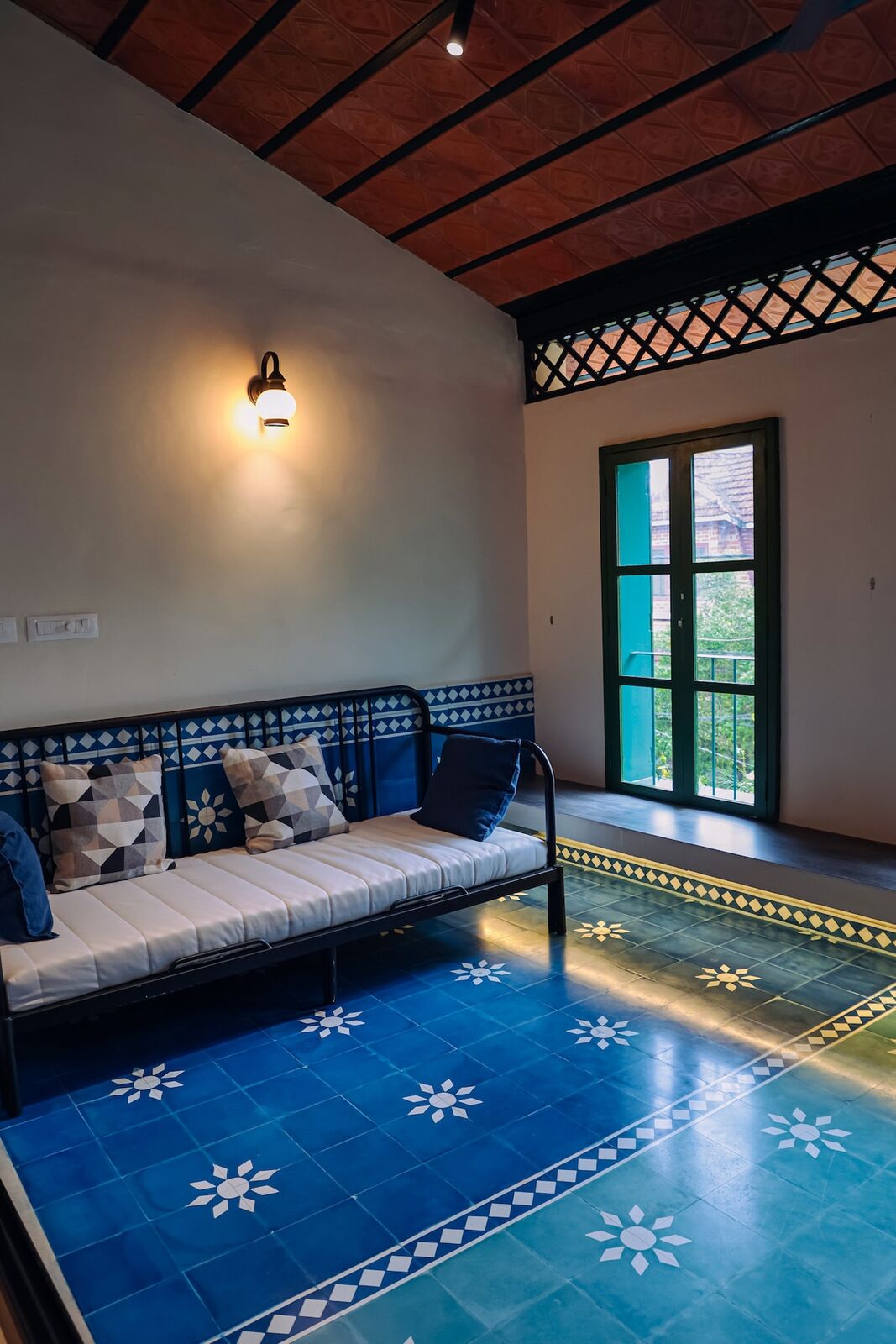 A cushioned bench on one of bedroom two's balconies, on blue and white patterned floor tiles under a pitched tile ceiling.
